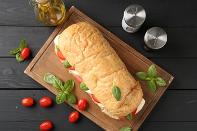 Photo of Tasty sandwich with mozzarella cheese, tomatoes, basil and spices on black wooden table, flat lay