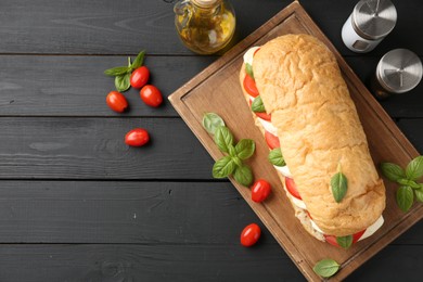 Photo of Tasty sandwich with mozzarella cheese, tomatoes, basil and spices on black wooden table, flat lay. Space for text