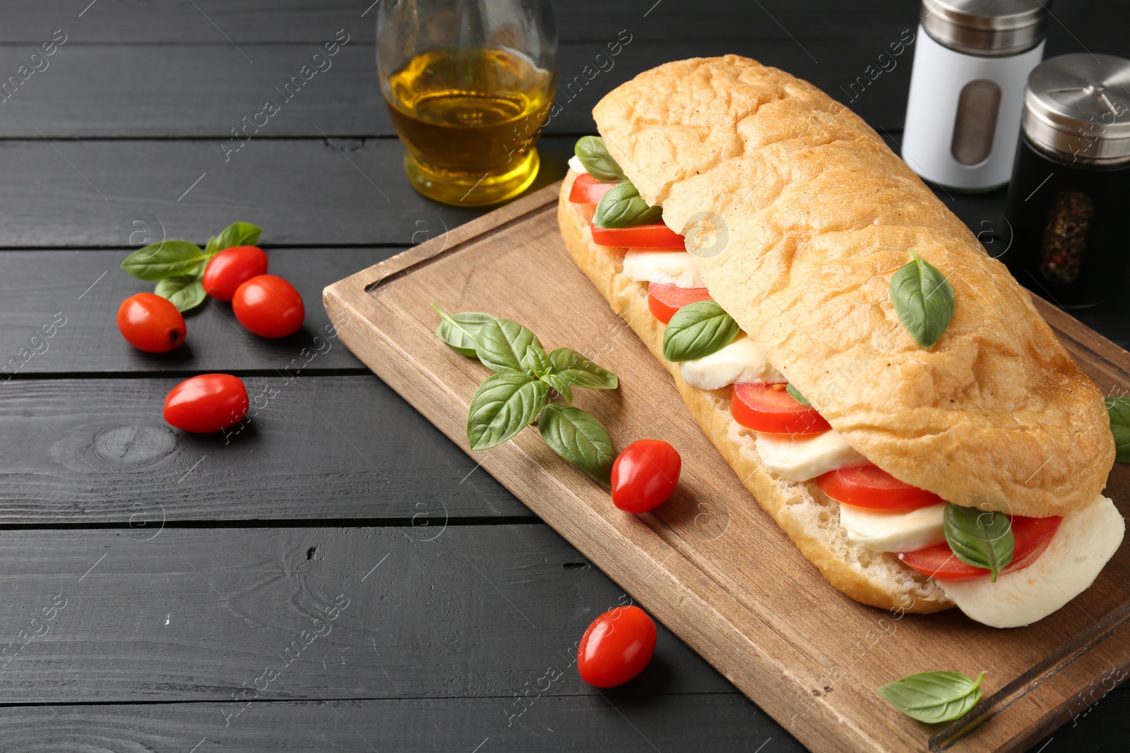 Tasty sandwich with mozzarella cheese, tomatoes and basil on black wooden table, closeup Photo of Tasty sandwich with mozzarella cheese, tomatoes and basil on black wooden table, closeup