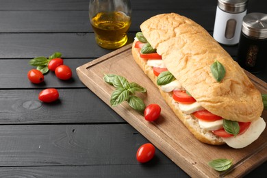 Photo of Tasty sandwich with mozzarella cheese, tomatoes and basil on black wooden table, closeup