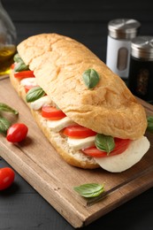 Photo of Tasty sandwich with mozzarella cheese, tomatoes and basil on black wooden table, closeup