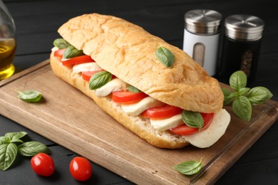 Photo of Tasty sandwich with mozzarella cheese, tomatoes and basil on black wooden table, closeup