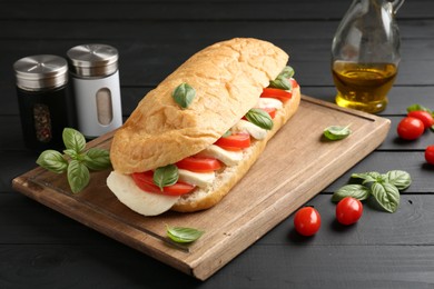 Photo of Tasty sandwich with mozzarella cheese, tomatoes and basil on black wooden table, closeup