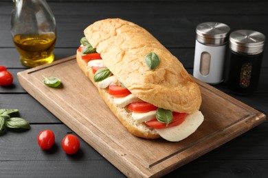 Photo of Tasty sandwich with mozzarella cheese, tomatoes and basil on black wooden table, closeup