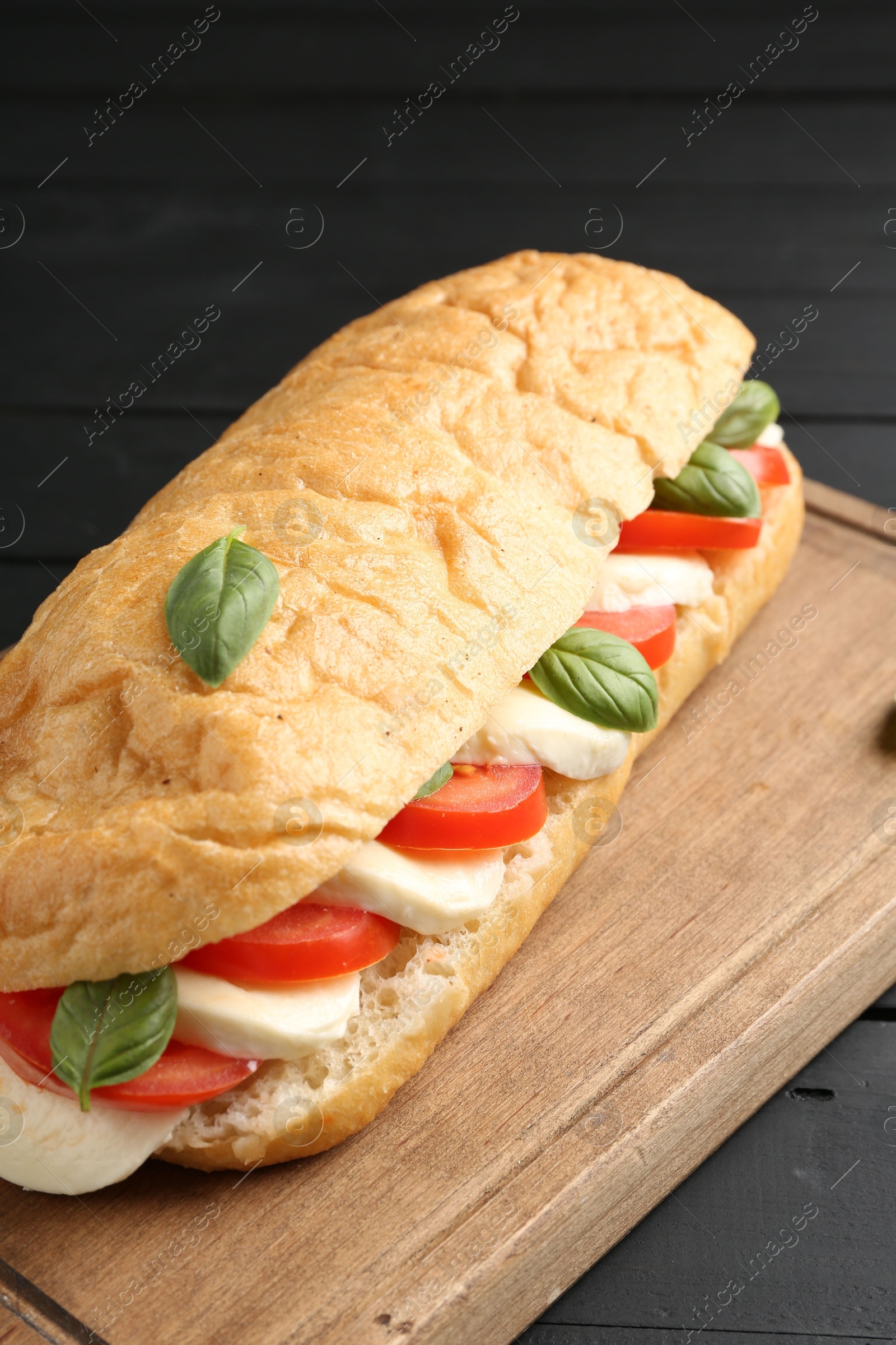 Tasty sandwich with mozzarella cheese, tomatoes and basil on black wooden table, closeup Photo of Tasty sandwich with mozzarella cheese, tomatoes and basil on black wooden table, closeup