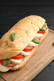Photo of Tasty sandwich with mozzarella cheese, tomatoes and basil on black wooden table, closeup