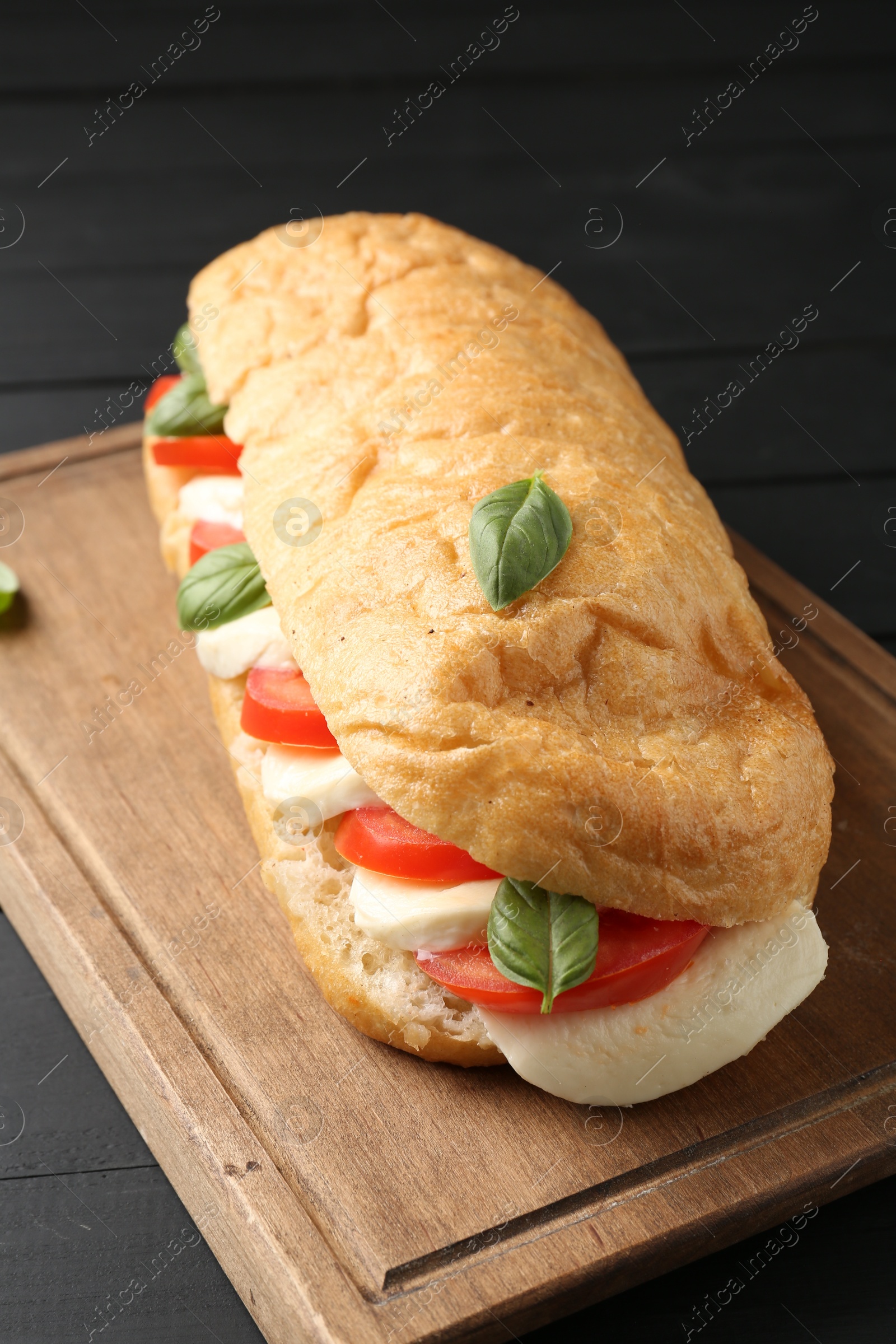 Tasty sandwich with mozzarella cheese, tomatoes and basil on black wooden table, closeup Photo of Tasty sandwich with mozzarella cheese, tomatoes and basil on black wooden table, closeup