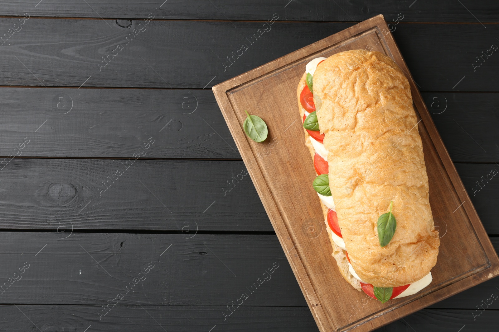 Tasty sandwich with mozzarella cheese, tomatoes and basil on black wooden table, top view. Space for text Photo of Tasty sandwich with mozzarella cheese, tomatoes and basil on black wooden table, top view. Space for text