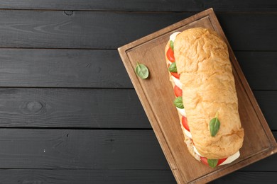 Photo of Tasty sandwich with mozzarella cheese, tomatoes and basil on black wooden table, top view. Space for text
