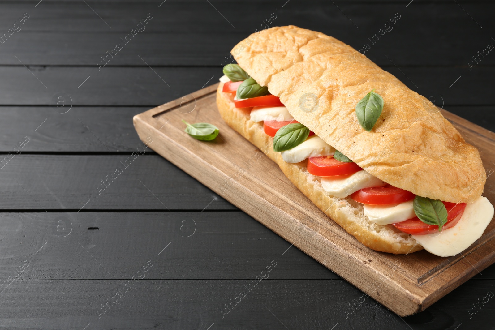 Tasty sandwich with mozzarella cheese, tomatoes and basil on black wooden table, closeup Photo of Tasty sandwich with mozzarella cheese, tomatoes and basil on black wooden table, closeup