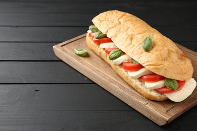 Photo of Tasty sandwich with mozzarella cheese, tomatoes and basil on black wooden table, closeup