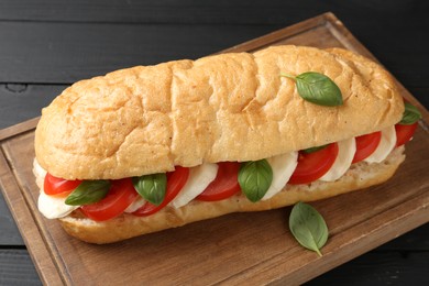 Photo of Tasty sandwich with mozzarella cheese, tomatoes and basil on black wooden table, closeup
