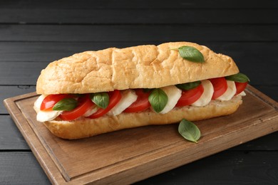 Photo of Tasty sandwich with mozzarella cheese, tomatoes and basil on black wooden table, closeup