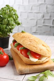 Photo of Tasty sandwich with mozzarella cheese, tomatoes and basil on light tiled table against grey textured wall, closeup