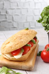 Photo of Tasty sandwich with mozzarella cheese, tomatoes and basil on light tiled table against grey textured wall, closeup