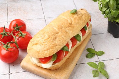 Photo of Tasty sandwich with mozzarella cheese, tomatoes and basil on light tiled table, closeup