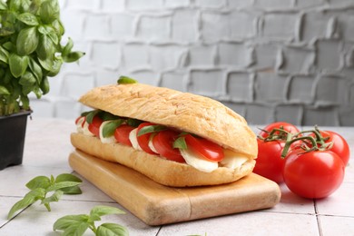 Photo of Tasty sandwich with mozzarella cheese, tomatoes and basil on light tiled table against grey textured wall, closeup