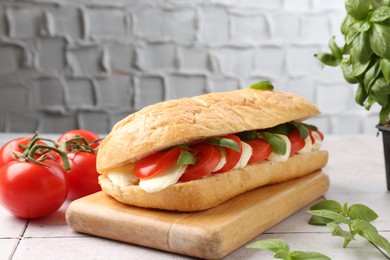 Photo of Tasty sandwich with mozzarella cheese, tomatoes and basil on light tiled table against grey textured wall, closeup