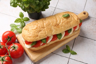 Photo of Tasty sandwich with mozzarella cheese, tomatoes and basil on light tiled table, closeup