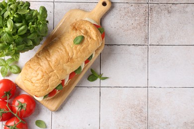 Photo of Tasty sandwich with mozzarella cheese, tomatoes and basil on light tiled table, flat lay. Space for text