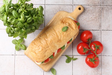 Photo of Tasty sandwich with mozzarella cheese, tomatoes and basil on light tiled table, flat lay