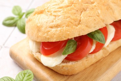Photo of Tasty sandwich with mozzarella cheese, tomatoes and basil on light tiled table, closeup