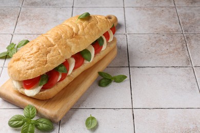 Photo of Tasty sandwich with mozzarella cheese, tomatoes and basil on light tiled table, closeup. Space for text