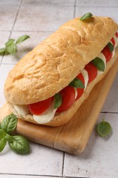 Photo of Tasty sandwich with mozzarella cheese, tomatoes and basil on light tiled table, closeup