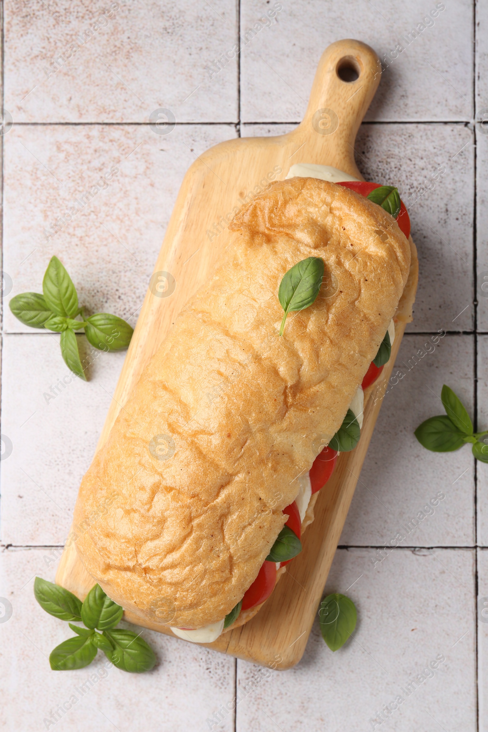 Photo of Tasty sandwich with mozzarella cheese, tomatoes and basil on light tiled table, flat lay
