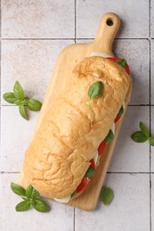 Photo of Tasty sandwich with mozzarella cheese, tomatoes and basil on light tiled table, flat lay