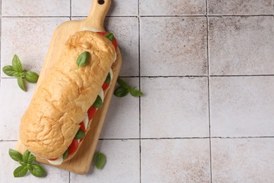 Photo of Tasty sandwich with mozzarella cheese, tomatoes and basil on light tiled table, flat lay. Space for text