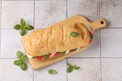 Photo of Tasty sandwich with mozzarella cheese, tomatoes and basil on light tiled table, flat lay
