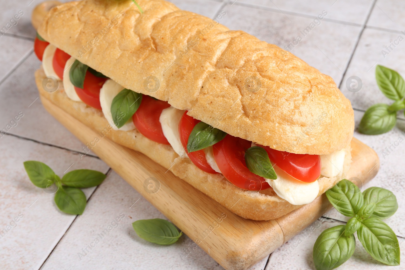 Tasty sandwich with mozzarella cheese, tomatoes and basil on light tiled table, closeup Photo of Tasty sandwich with mozzarella cheese, tomatoes and basil on light tiled table, closeup