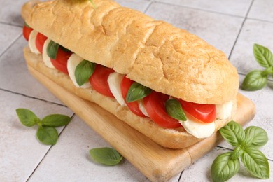 Photo of Tasty sandwich with mozzarella cheese, tomatoes and basil on light tiled table, closeup