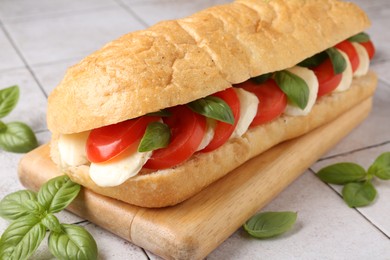 Photo of Tasty sandwich with mozzarella cheese, tomatoes and basil on light tiled table, closeup