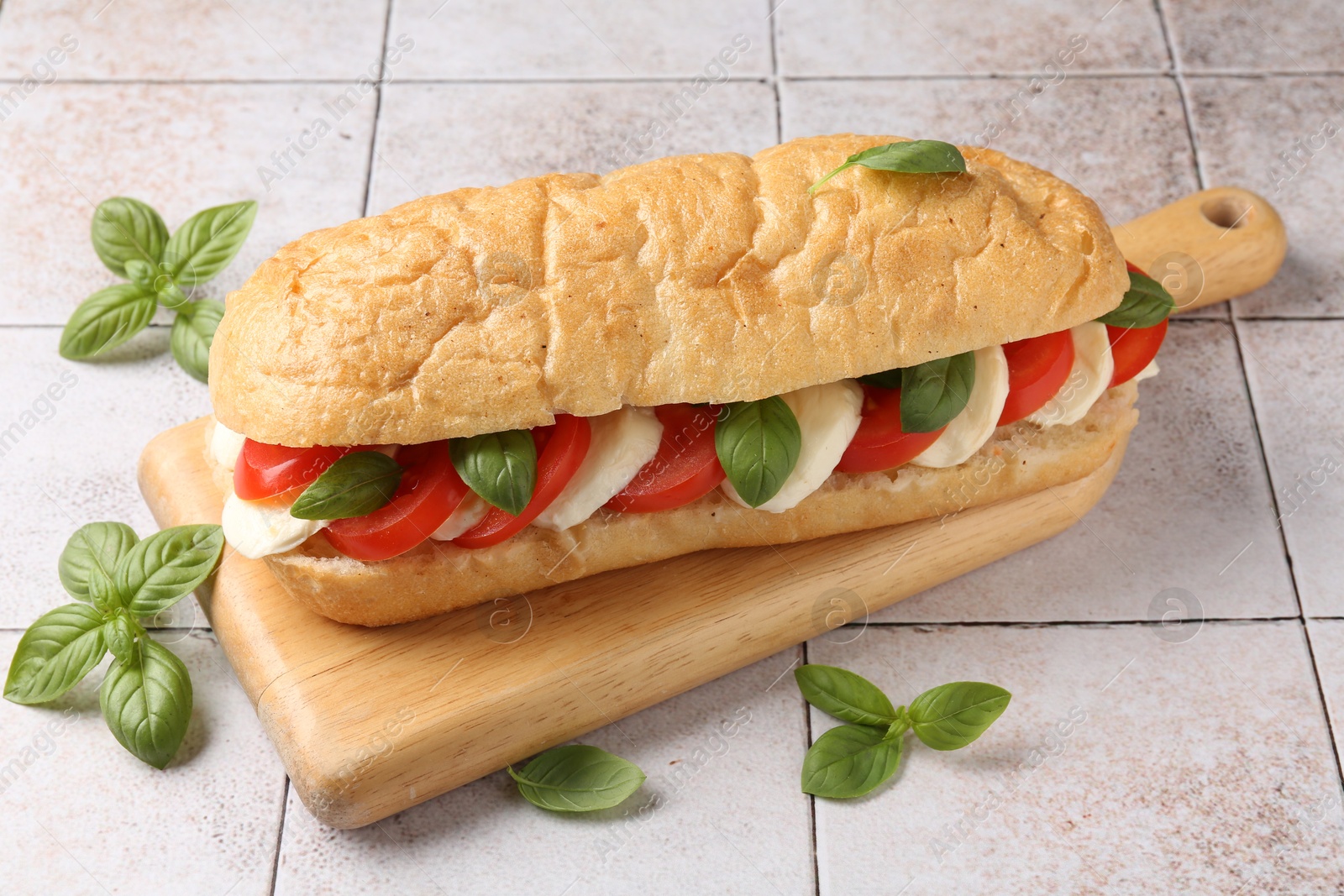 Tasty sandwich with mozzarella cheese, tomatoes and basil on light tiled table, closeup Photo of Tasty sandwich with mozzarella cheese, tomatoes and basil on light tiled table, closeup