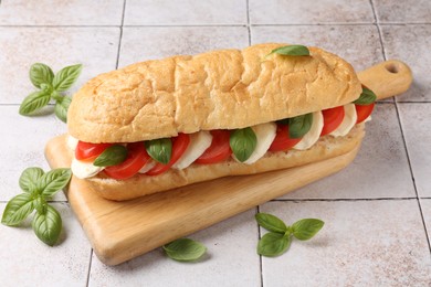 Photo of Tasty sandwich with mozzarella cheese, tomatoes and basil on light tiled table, closeup
