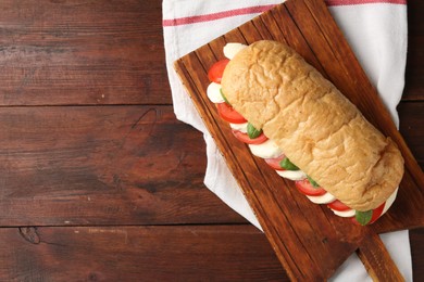 Photo of Tasty sandwich with mozzarella cheese, tomatoes and basil on wooden table, top view. Space for text