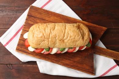 Photo of Tasty sandwich with mozzarella cheese, tomatoes and basil on wooden table, top view