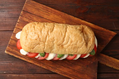 Photo of Tasty sandwich with mozzarella cheese, tomatoes and basil on wooden table, top view