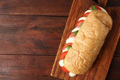 Photo of Tasty sandwich with mozzarella cheese, tomatoes and basil on wooden table, top view. Space for text