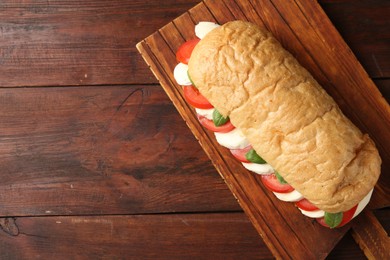 Photo of Tasty sandwich with mozzarella cheese, tomatoes and basil on wooden table, top view. Space for text