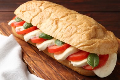 Photo of Tasty sandwich with mozzarella cheese, tomatoes and basil on wooden table, closeup