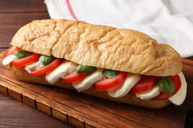 Photo of Tasty sandwich with mozzarella cheese, tomatoes and basil on wooden table, closeup