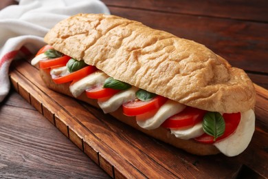 Photo of Tasty sandwich with mozzarella cheese, tomatoes and basil on wooden table, closeup