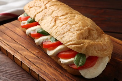 Photo of Tasty sandwich with mozzarella cheese, tomatoes and basil on wooden table, closeup