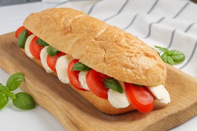Photo of Tasty sandwich with mozzarella cheese, tomatoes and basil on white table, closeup