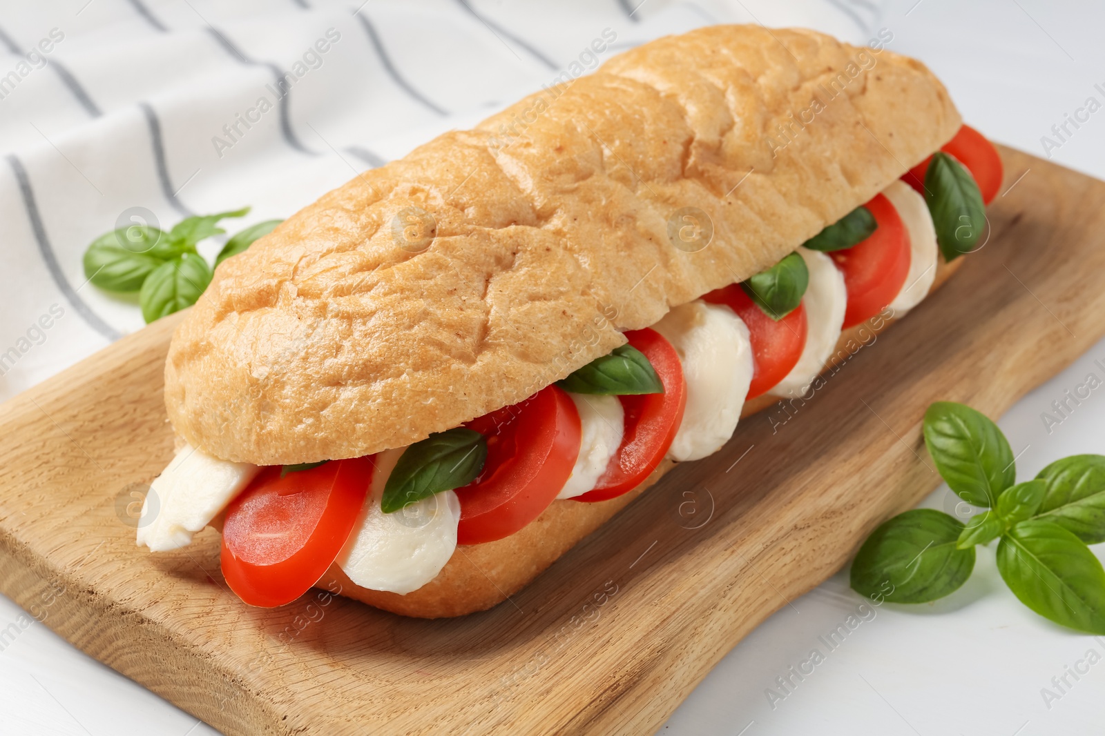 Tasty sandwich with mozzarella cheese, tomatoes and basil on white table, closeup Photo of Tasty sandwich with mozzarella cheese, tomatoes and basil on white table, closeup