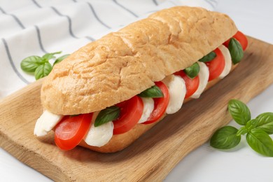 Photo of Tasty sandwich with mozzarella cheese, tomatoes and basil on white table, closeup
