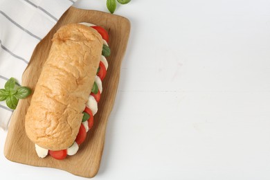 Photo of Tasty sandwich with mozzarella cheese, tomatoes and basil on white wooden table, flat lay. Space for text
